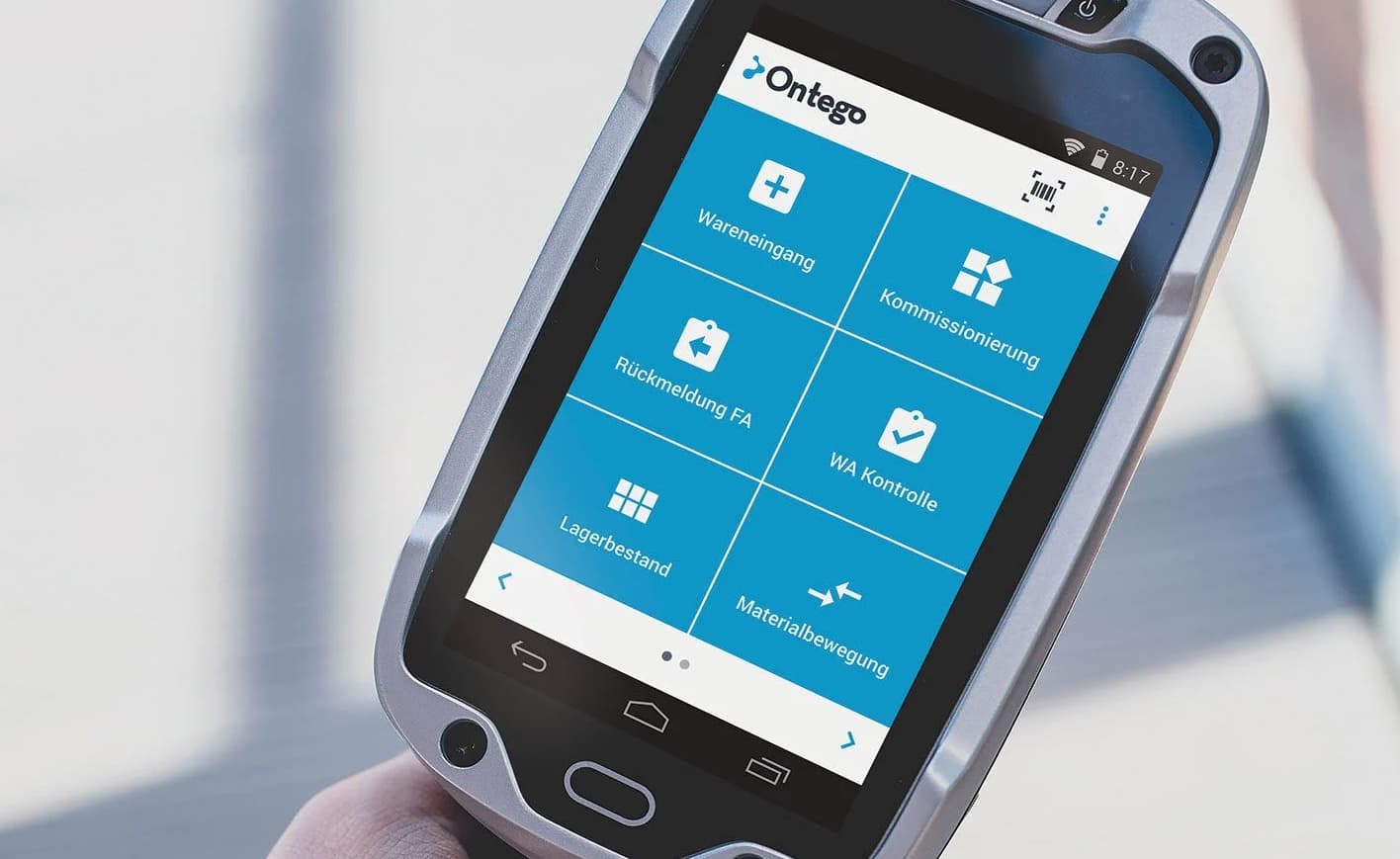 A close-up of a hand holding a rugged mobile device displaying the Ontego logistics app menu with various warehouse functions in German.