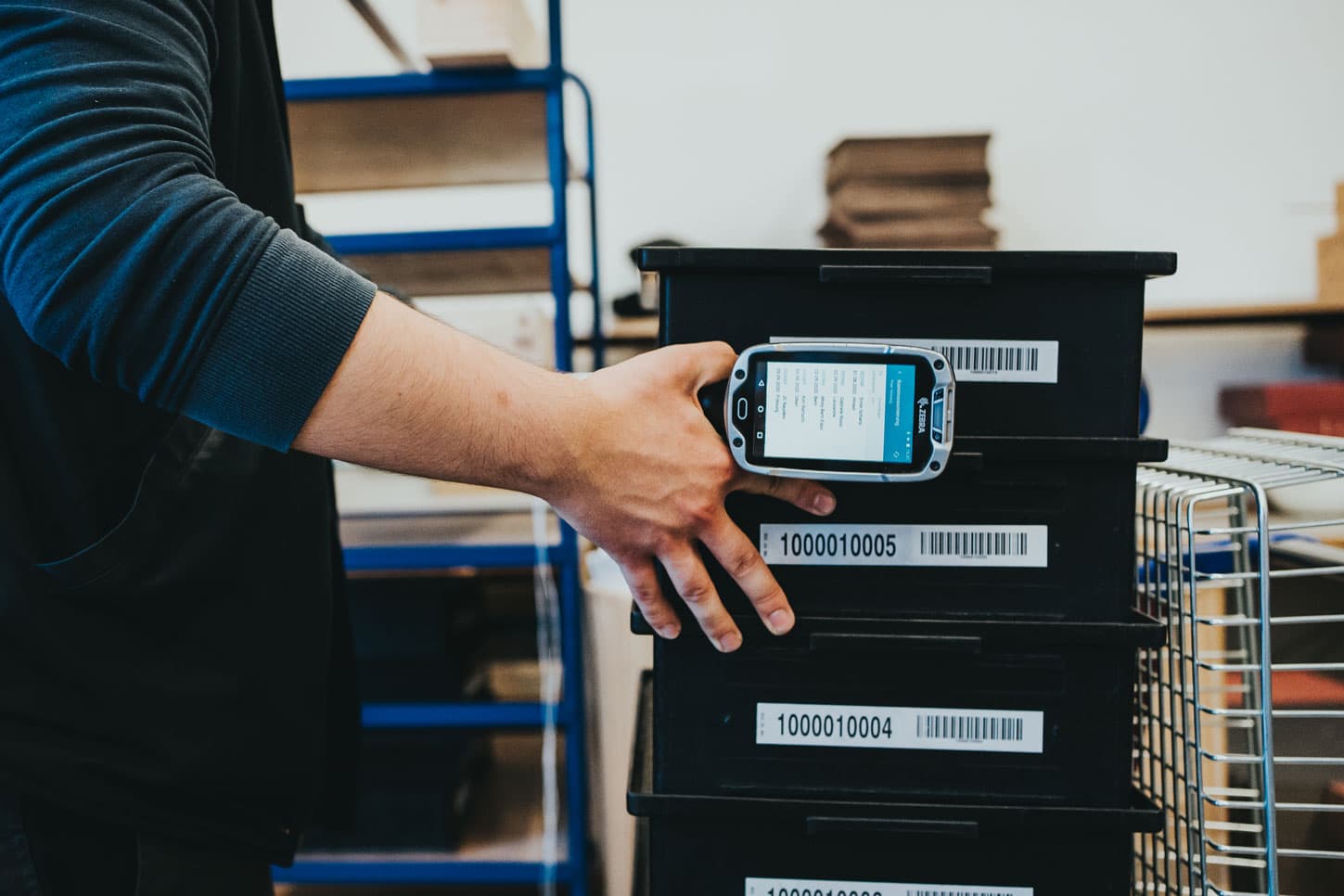 Warehouse worker scanning labeled storage bins with a mobile barcode scanner.