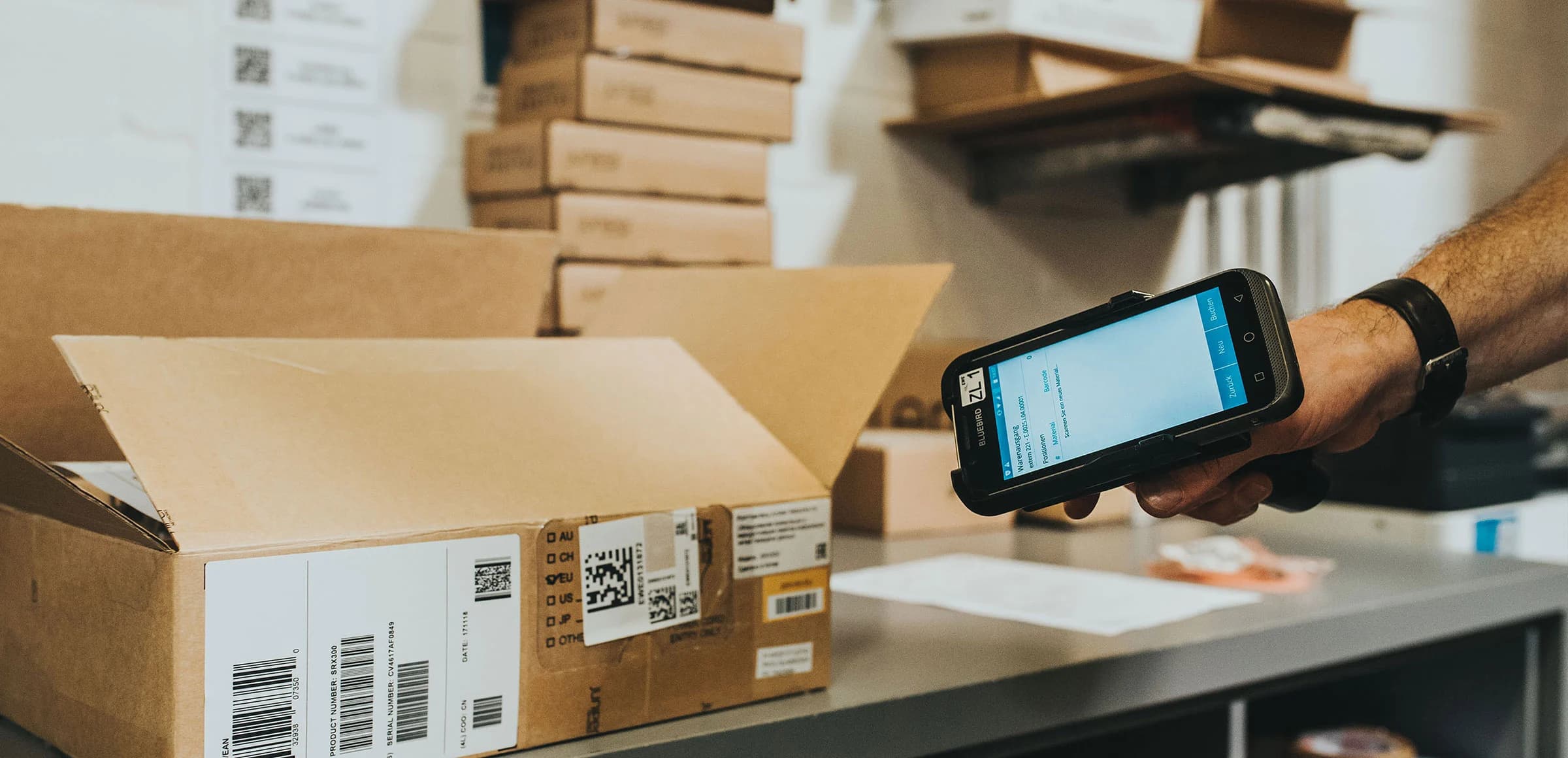 Warehouse worker using a Bluebird Android handheld scanner with Ontego SAP logistics app to capture barcode data from a shipping box for mobile data entry.
